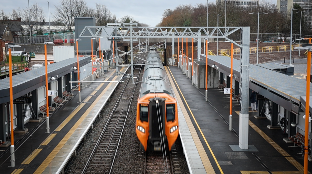 A view overlooking the track with yellow fronted train passing between two platforms on a new empty station